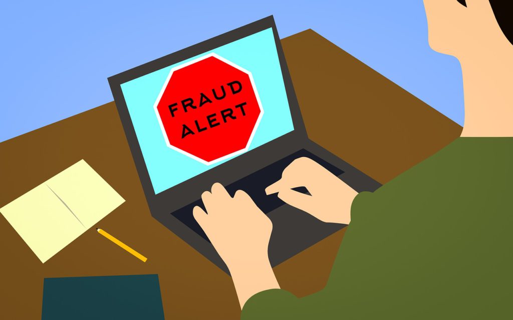 A rendered image of a person sitting at a laptop with a large stop sign on screen. The sign reads "fraud alert". These sorts of screen hijacking pop-ups are often used in antivirus scams. 